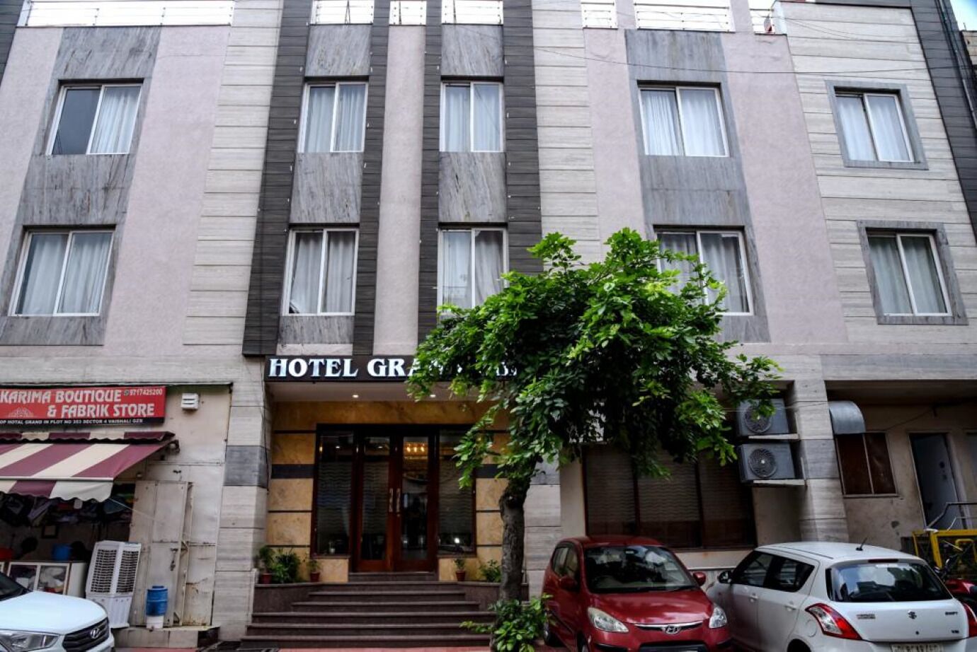 Un hotel con facciata moderna, ingresso ben visibile con gradini e auto parcheggiate davanti.