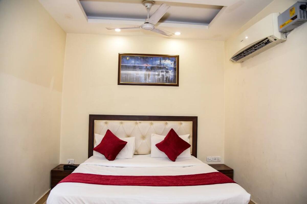 Habitación de hotel con una cama, ventilador de techo, unidad de aire acondicionado y un cuadro en la pared.