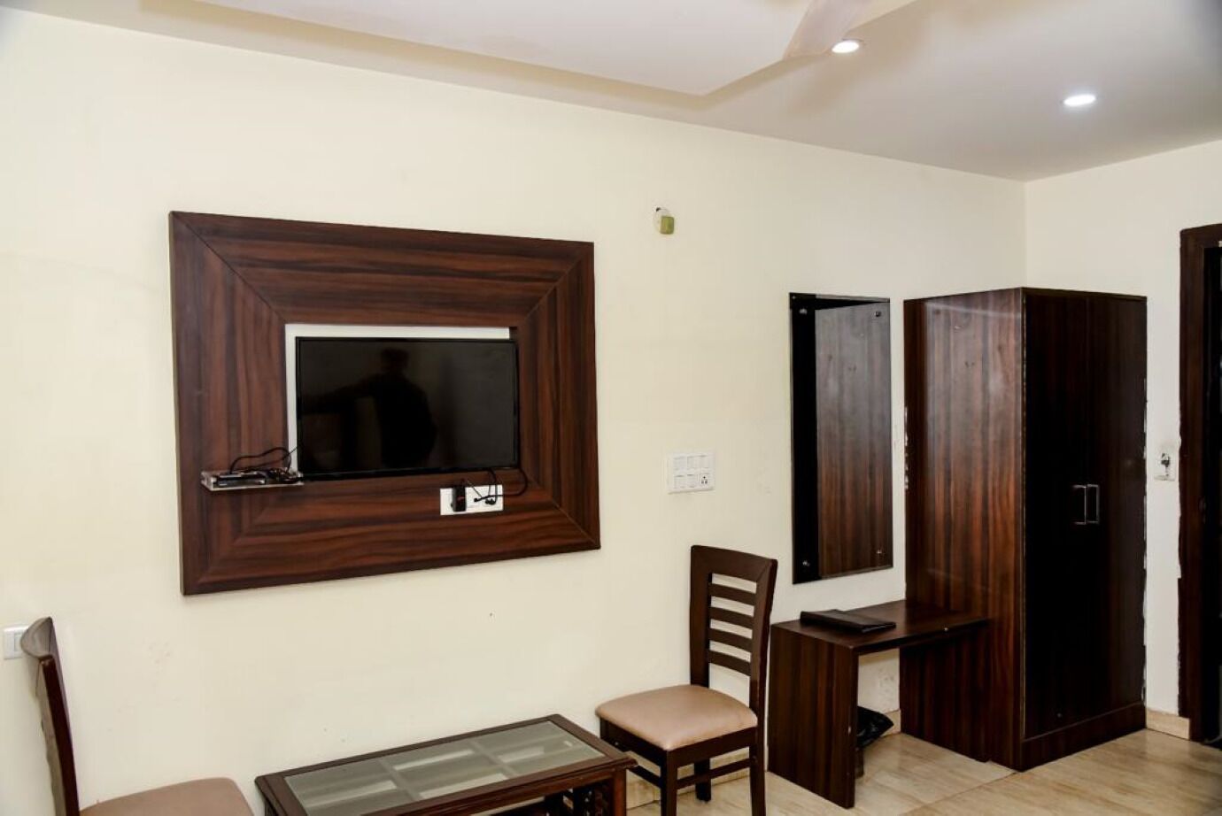 A room with a wooden TV stand, a wooden chair, a small table, and a wardrobe.