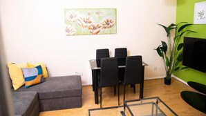 Un salon avec un canapé, une table à manger et des chaises, un tableau accroché au mur et un mur de couleur verte.
