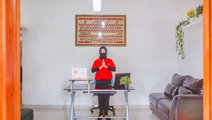 A person standing at a reception desk with a laptop, a framed sign on the wall, and a couch in the background. - Hotel O Wisma Bambu Syariah (Bandar Lampung)