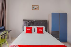 Una camera da letto con un letto, due cuscini rossi, una testiera grigia, un armadio blu e una piccola cornice con un'immagine appesa al muro.