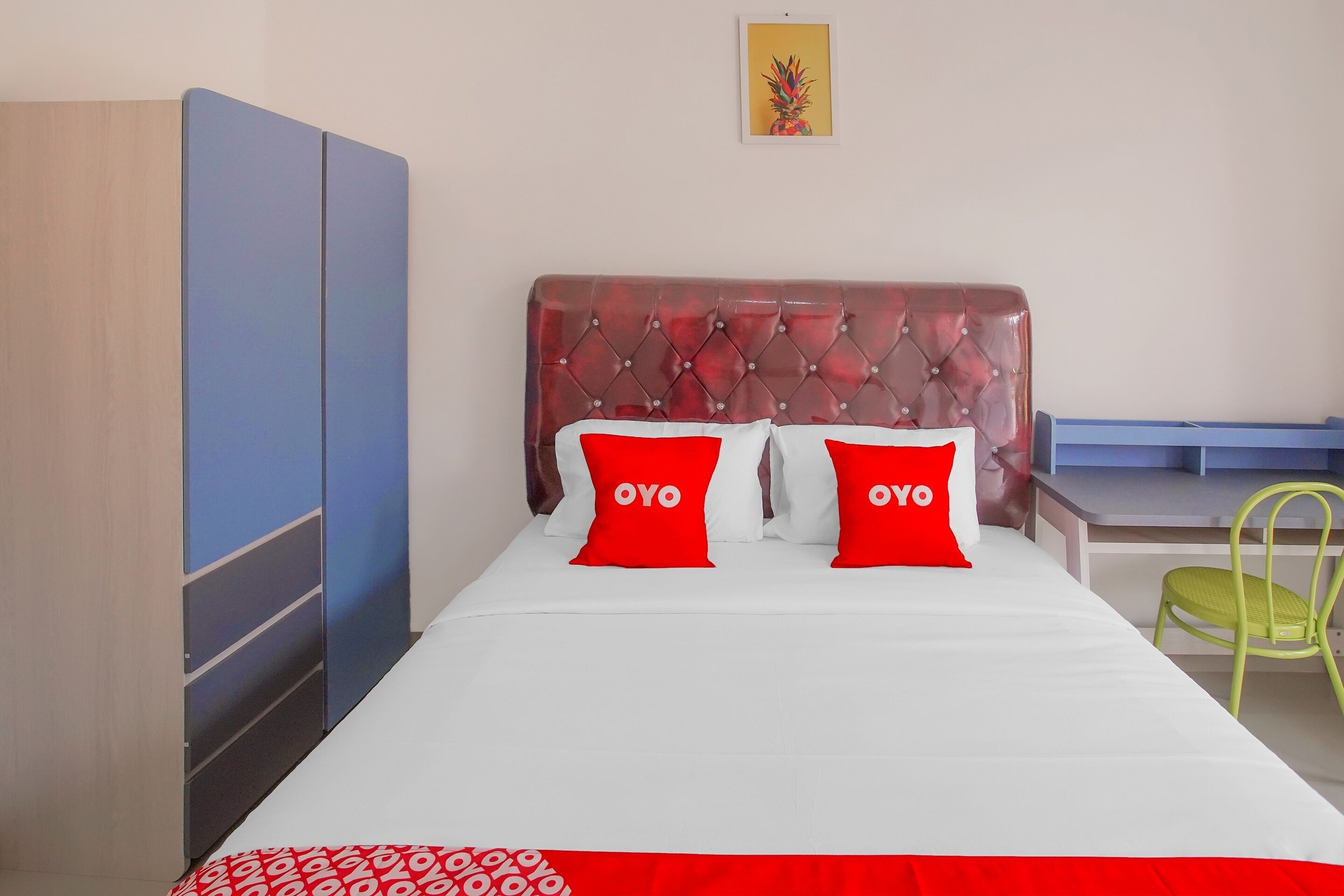 A bed with a tufted headboard, two red pillows with the word "OYO" on them, a green chair, and a blue wardrobe.