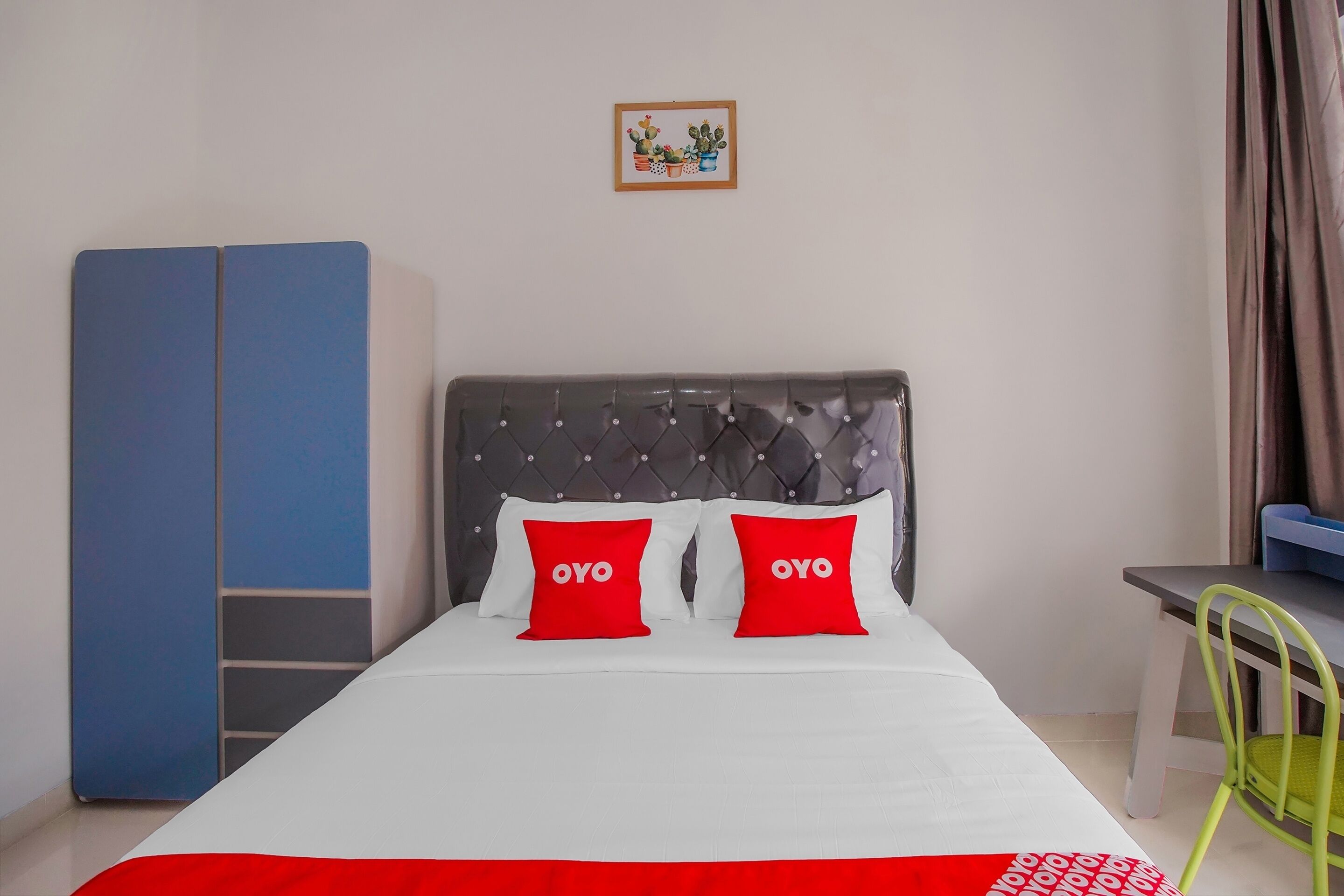 Una cama con dos almohadas rojas, un cabecero gris y una colcha blanca.