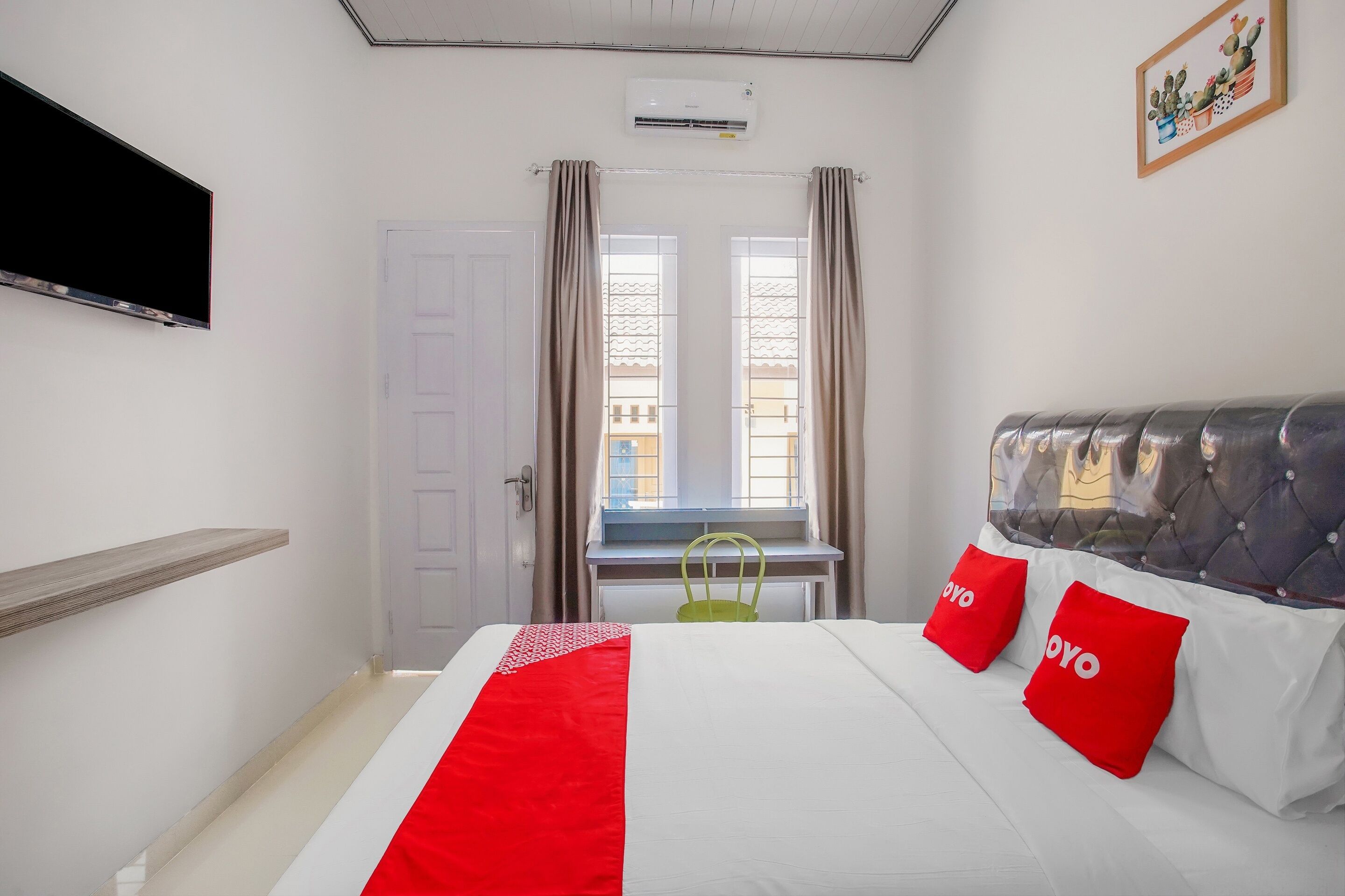 Een hotelkamer met een bed, een aan de muur bevestigde televisie, een raam met gordijnen en een stoel bij het raam.