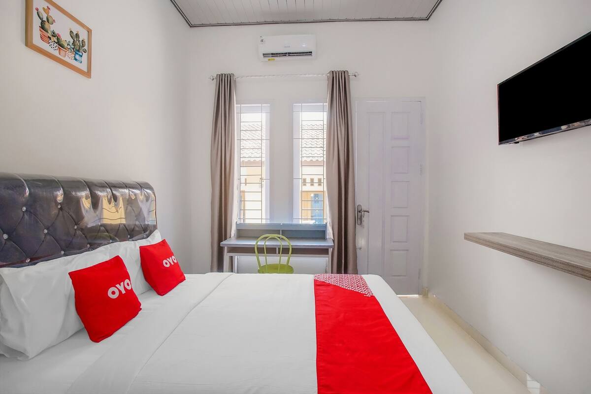 A hotel room with a bed, a television mounted on the wall, a window with curtains, and a door.