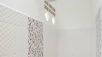 Casa de banho com sanita, chuveiro com duche manual e secador de cabelo fixado na parede.