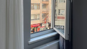 Une fenêtre donnant sur un immeuble à plusieurs étages, un radiateur en dessous et une porte entrouverte sur la droite.