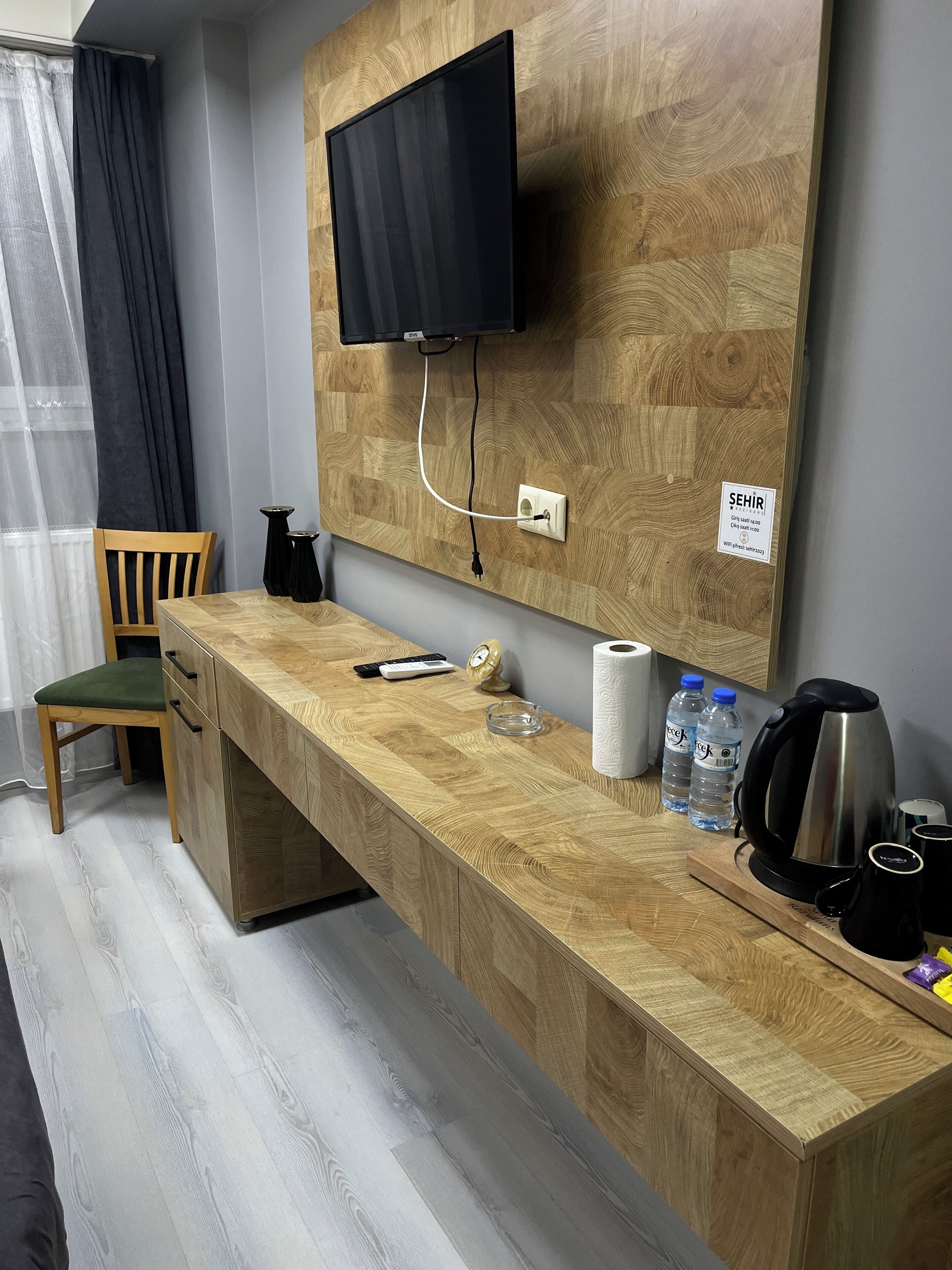 A wooden desk with a flat-screen TV mounted above it, a chair, a small cabinet, and a coffee maker.