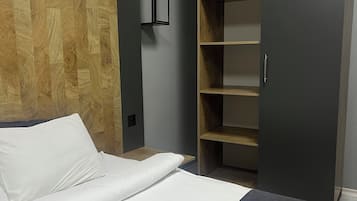 Quarto de hotel moderno com parede em madeira, cama com roupa de cama branca, guarda-roupa cinza e estante embutida.