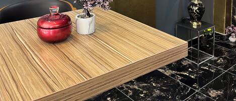 Una habitación moderna con una mesa de madera, un florero rojo, una planta en maceta, un adorno en la pared y una lámpara negra y dorada.