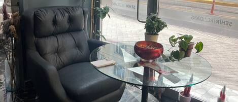 A modern room with a black leather chair, a glass table with a red bowl, and a painting of a landscape.