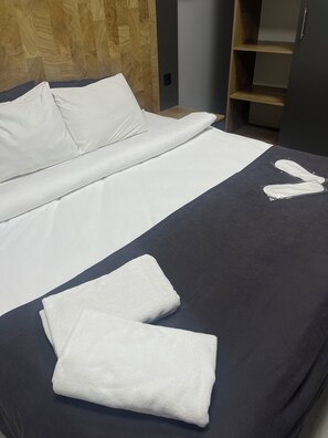 A neatly made bed with white linens and two folded towels on a dark blue bedspread. - Şehir Rezidans (Eskisehir)