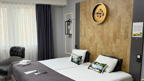 Une chambre d’hôtel moderne avec un grand lit, une table de chevet, une chaise et une fenêtre avec des rideaux.