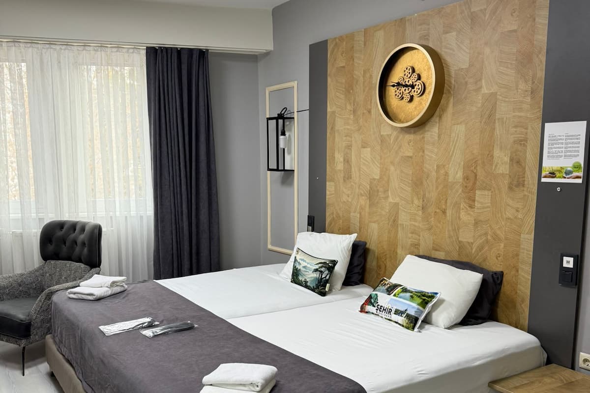 Une chambre d’hôtel moderne avec un grand lit, une table de chevet, une chaise et une fenêtre avec des rideaux.