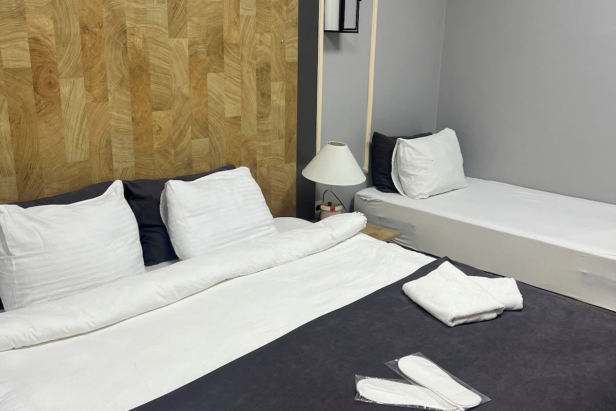 Une chambre d’hôtel avec un grand lit, un lit plus petit, une table de chevet avec une lampe et une tête de lit en bois.