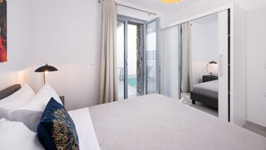 Een moderne hotelkamer met een groot bed, een nachtkastje met een lamp, een glazen schuifdeur naar een balkon en een grote spiegel aan de muur.