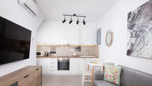 Een moderne keuken met witte kasten, een inbouwoven en een zithoek met een grijze bank en een kleine ronde tafel.