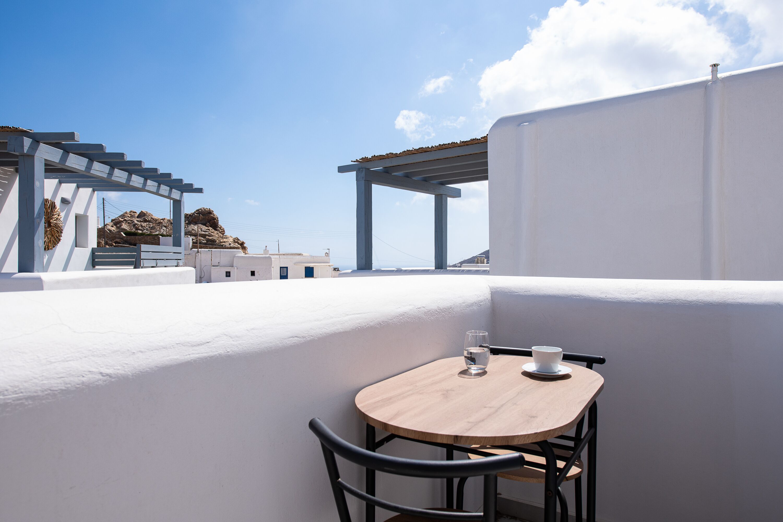 A rooftop terrace with a wooden table and chairs, a white wall, and a clear blue sky.