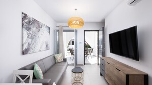 Een moderne woonkamer met een grijze bank, een ronde salontafel, een houten kast en een flatscreen televisie aan de muur.