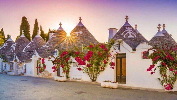 A row of traditional stone-roofed buildings with white walls and pink flowering plants in front. - Casa Ojala' in the Center of Alberobello (Alberobello)