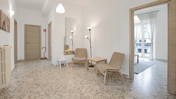 A modern living room with a stone floor, a wooden door, a white table, a chair, and a floor lamp.