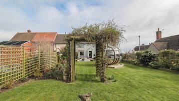 A well-maintained garden with a stone sculpture in the foreground, a wooden pergola, and a spherical metal sculpture.
