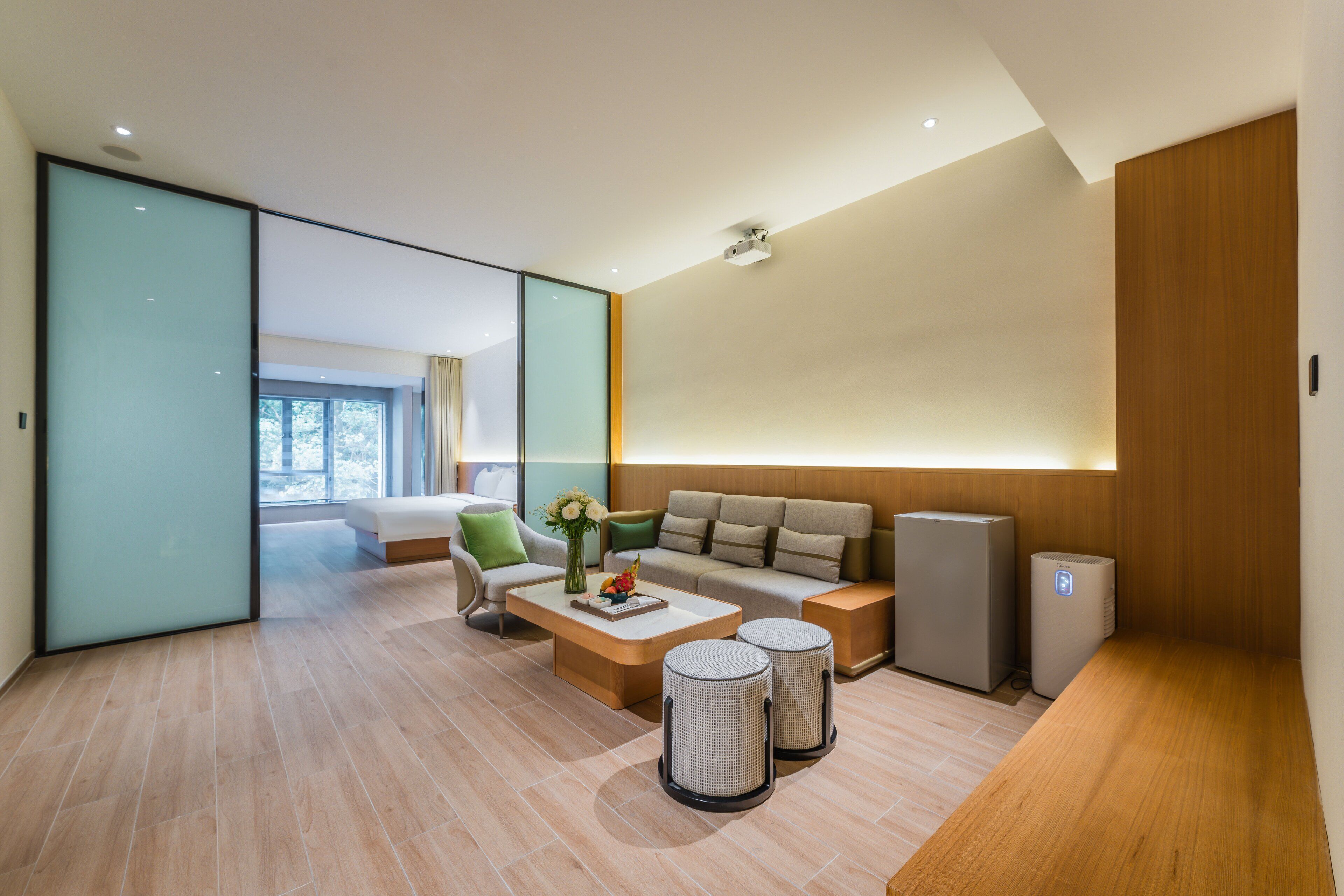A modern hotel room with a sofa, a coffee table, two waste baskets, and a small heater.