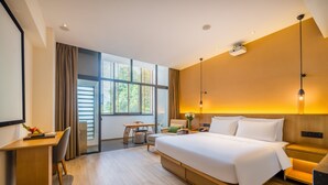 A modern hotel room with a large bed, a desk, a chair, and a view of the outdoors through large windows. - Holiday Inn Wuyi Mountain Water Village by IHG (Nanping)