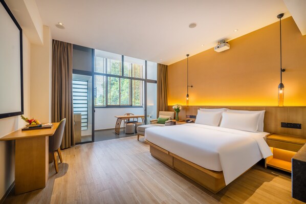 A modern hotel room with a large bed, a desk, a chair, and a view of the outdoors through large windows. - Holiday Inn Wuyi Mountain Water Village by IHG (Nanping)