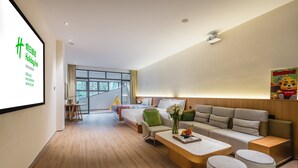 A modern hotel room with a large bed, a sofa, a coffee table, and a TV screen displaying the hotel name. - Holiday Inn Wuyi Mountain Water Village by IHG (Nanping)