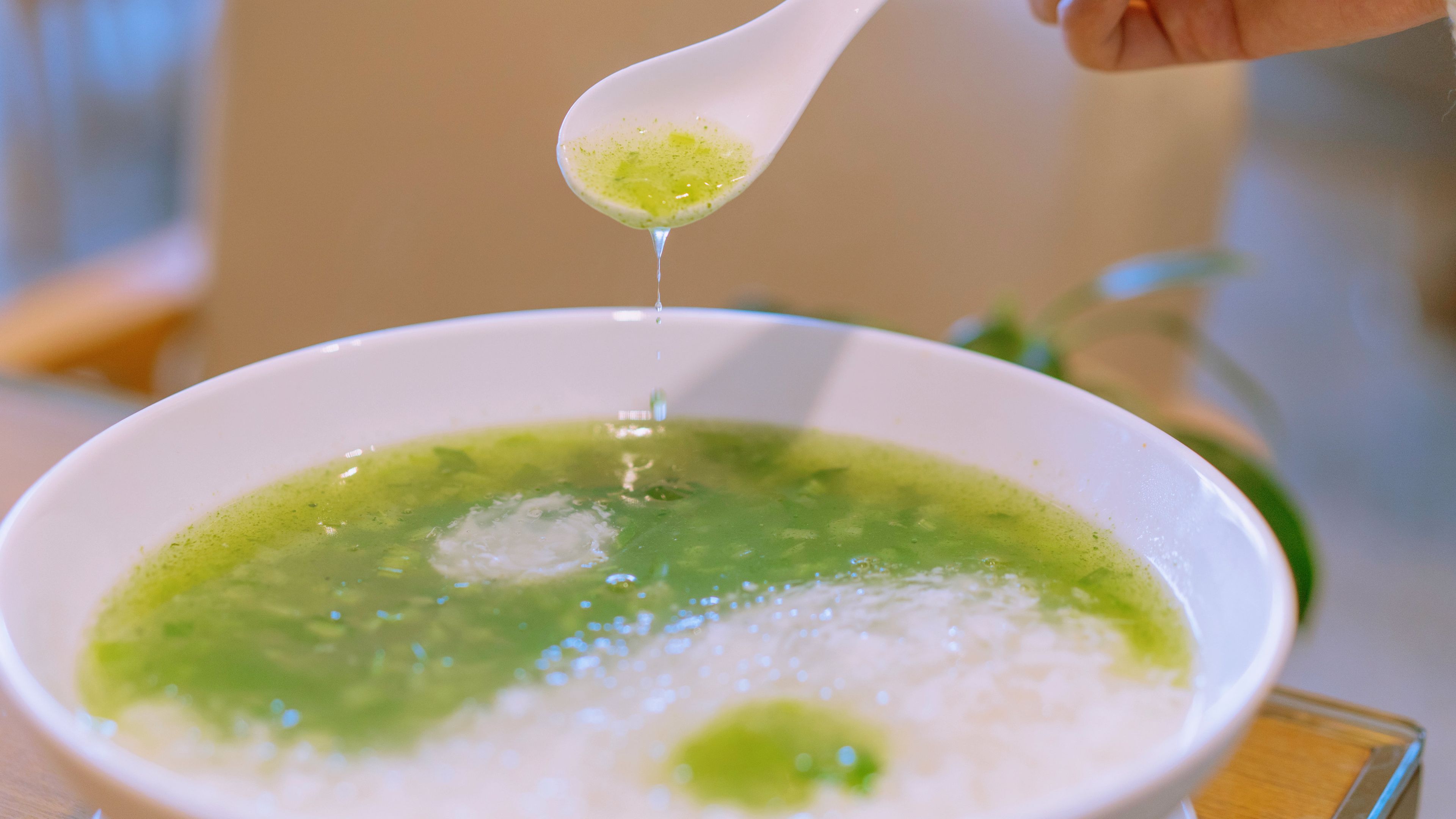Un tazón de sopa verde con líquido transparente siendo servido.