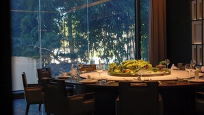 A round dining table with chairs, a centerpiece, and a view of trees through large windows. - Holiday Inn Wuyi Mountain Water Village by IHG (Nanping)