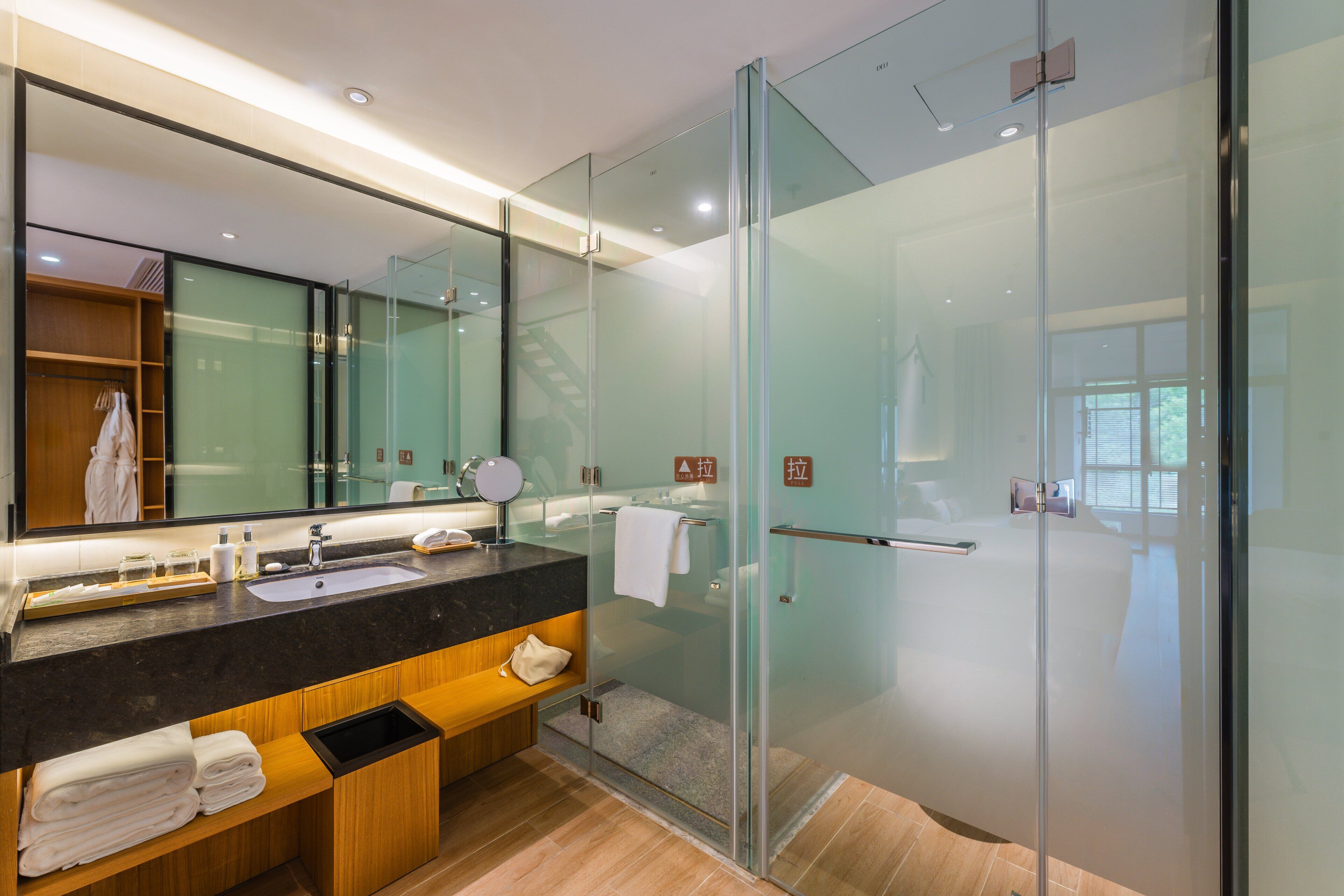Un baño moderno con ducha de vidrio, un espejo grande y un tocador de madera con toallas.