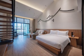 Habitación de hotel moderna con una cama grande, una zona de estar con una silla y una mesita, un ventanal amplio y una escalera que lleva a un espacio al aire libre.