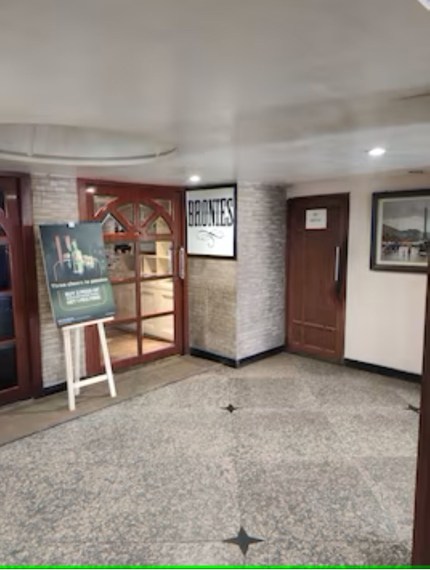 A hotel lobby with a stone floor, a framed sign reading "BRONTES," and a wooden door.