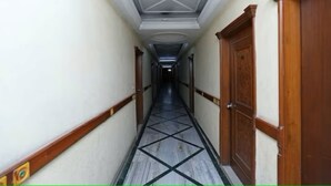A hallway with a tiled floor, wooden doors, and a white ceiling with a geometric pattern. - Revking at Hotel Batra  (Ambala)