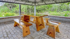 A wooden picnic table with benches under a covered area with a view of greenery. - Hotel O Homestay Pasir Padi Permai Syariah (Pangkalpinang)