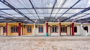 A covered outdoor area with a brick floor, featuring a row of buildings with red and yellow walls and multiple doors. - Hotel O Homestay Pasir Padi Permai Syariah (Pangkalpinang)