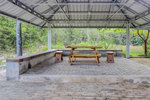 A covered outdoor seating area with a picnic table and benches, surrounded by a brick floor and concrete steps. - Hotel O Homestay Pasir Padi Permai Syariah (Pangkalpinang)