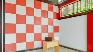 A room with a checkered red and white wall, a wooden desk with a laptop and a white sign, and a window with a metal grill. - OYO Life 3982 Azka Homestay Syariah (Bandar Lampung)