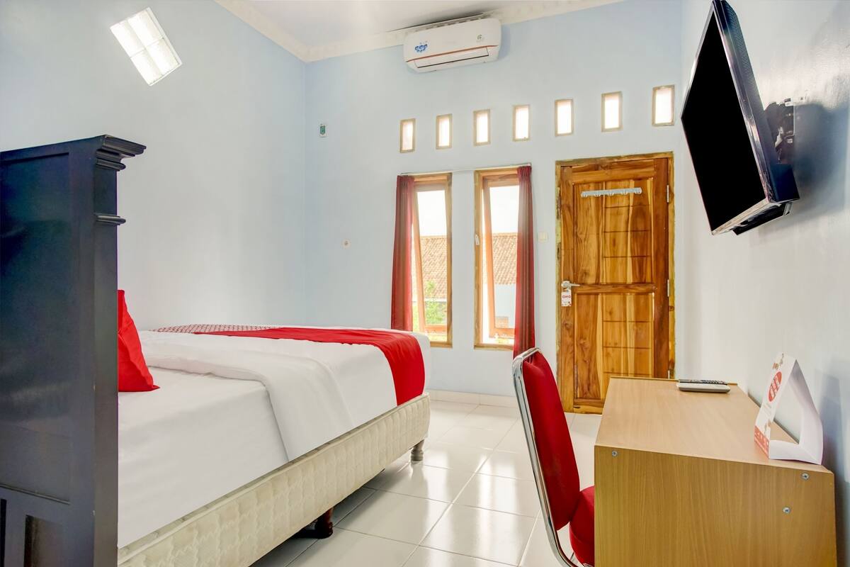 A hotel room with a bed, a desk, a chair, a TV, and a wooden door.