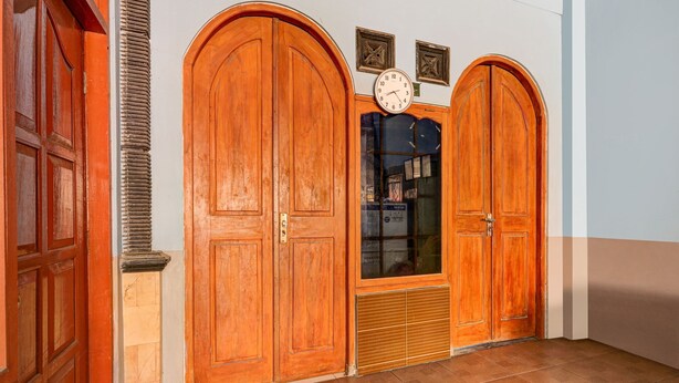 A hallway with two wooden double doors, a clock, and a small window with blinds.