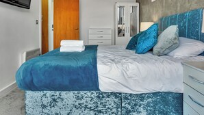 A bedroom with a bed, a dresser, a TV, and a door. - 2 Bed Penthouse-sleeps 4 With Wraparound Balcony (Birmingham)