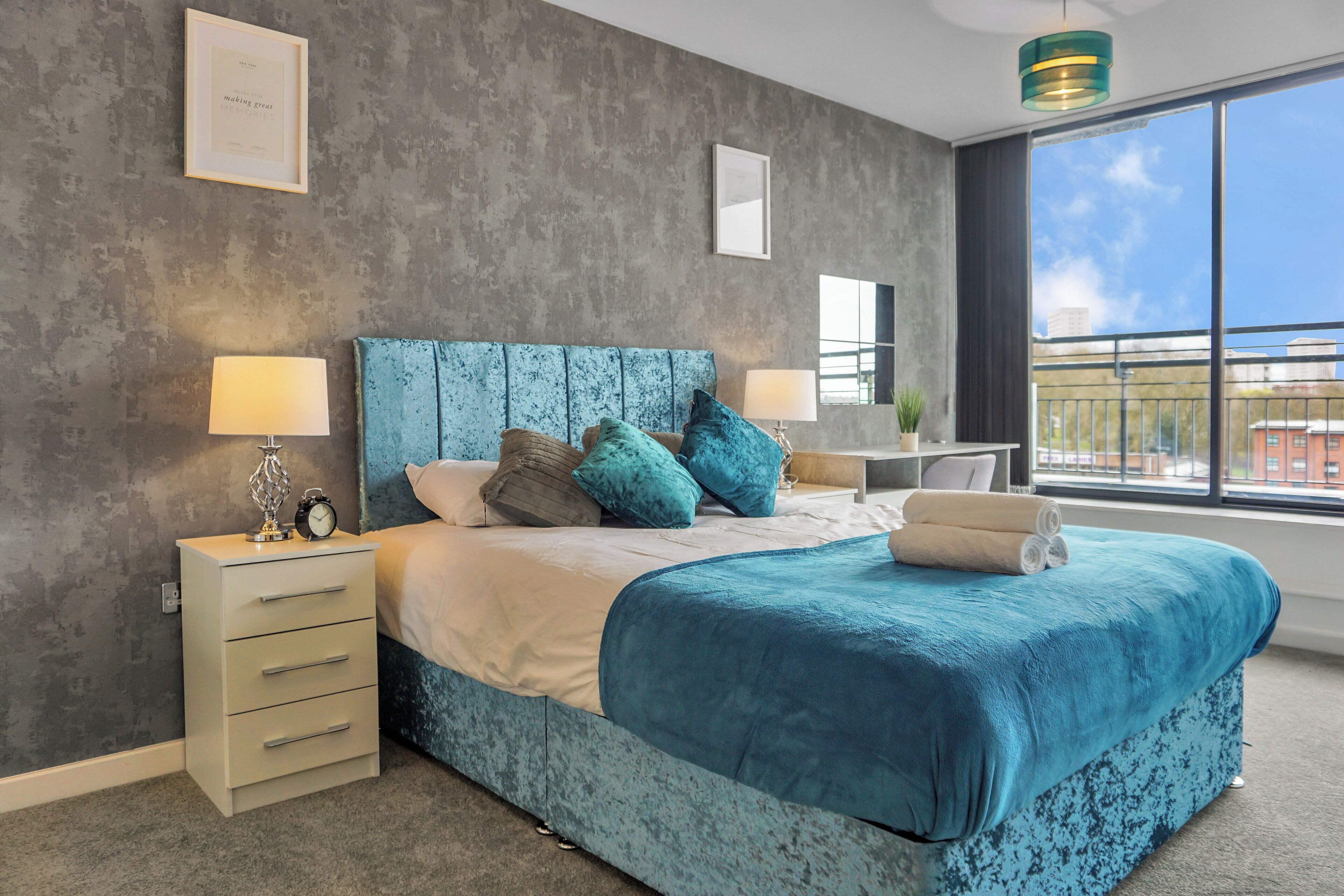 A modern bedroom with a large bed, two bedside tables, a nightstand, and a view of the city through large windows.