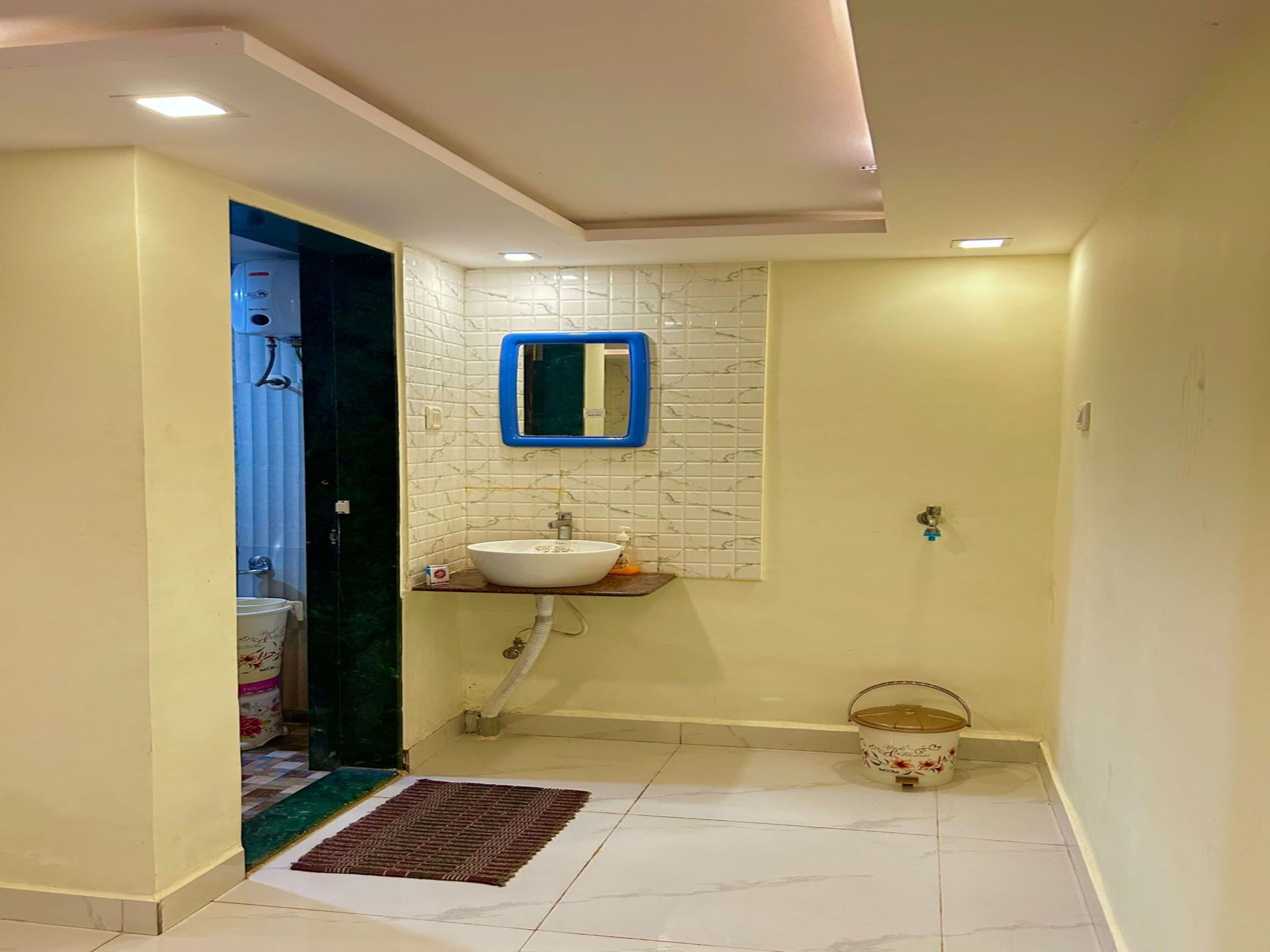 Un baño con un lavamanos blanco, un espejo con marco azul, una pared de azulejos blancos y un balde blanco pequeño en el suelo.