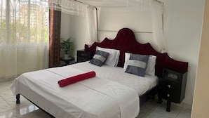 Un lit bien fait, recouvert d’une courtepointe blanche et agrémenté d’un coussin rouge, avec une tête de lit rouge et un baldaquin au-dessus.
