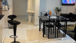 Un salon moderne avec un coin repas, un téléviseur fixé au mur et une cuisine visible au fond.