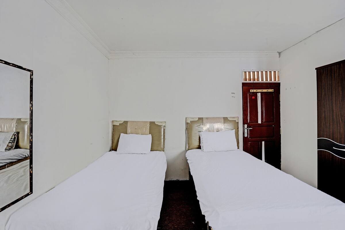 Une chambre avec deux lits simples, une porte en bois et un miroir sur le mur de gauche.