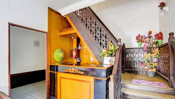 A reception area with a wooden counter, a staircase with a decorative railing, and a flower arrangement on the landing.